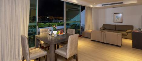 A modern living room with a dining area, large windows, and a view of the city at night.