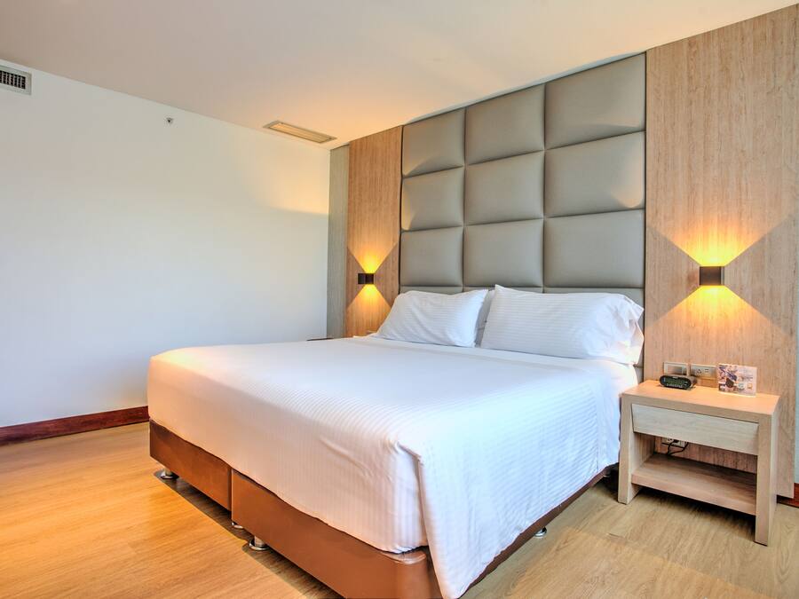 Una cama bien hecha con cabecera, mesitas de noche con lámparas y suelo de madera.
