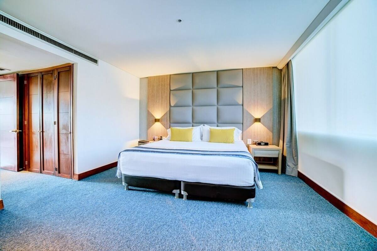 Ein Hotelzimmer mit einem großen Bett, einem gepolsterten Kopfteil, zwei Nachttischen mit Lampen und einem Teppichboden.