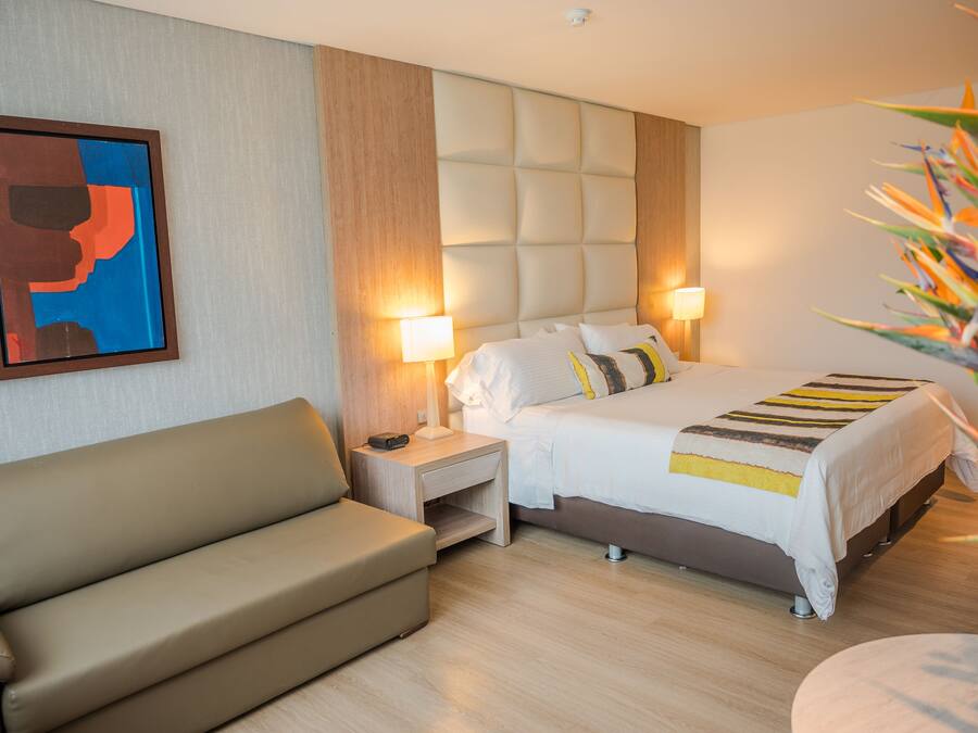 A hotel room with a bed, a sofa, a nightstand, and a lamp.