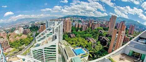 Un edificio alto con piscina y zona de descanso en la azotea, rodeado de un denso paisaje urbano y vegetación.
