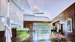 Un vestíbulo de hotel con una recepción, una araña de cristal, un piano y un espejo grande.