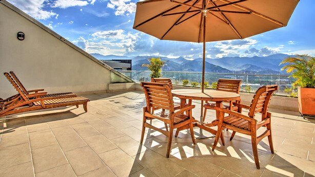 Eine Terrasse mit Tisch und Stühlen, einem großen Sonnenschirm und Blick auf die Berge.