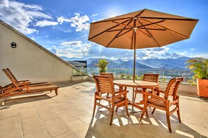 A terrace with a table and chairs, a large umbrella, and a view of mountains.