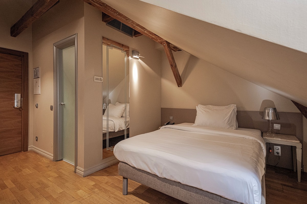 A bedroom with a bed, bedside table, lamp, and a door leading to a bathroom.