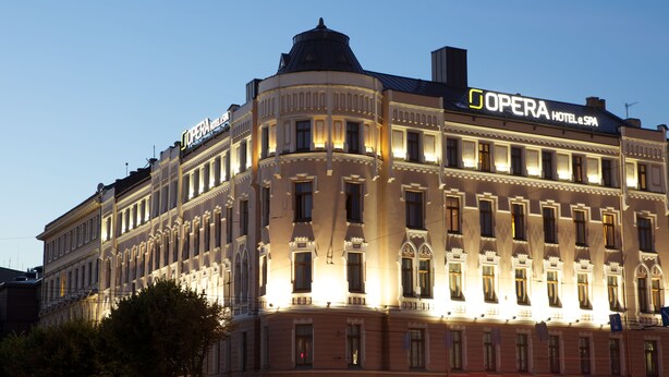Un grand bâtiment historique, sur lequel on peut voir une enseigne bien visible indiquant « Hôtel et spa de l’Opéra ». Il présente des éléments architecturaux classiques et est illuminé au crépuscule.