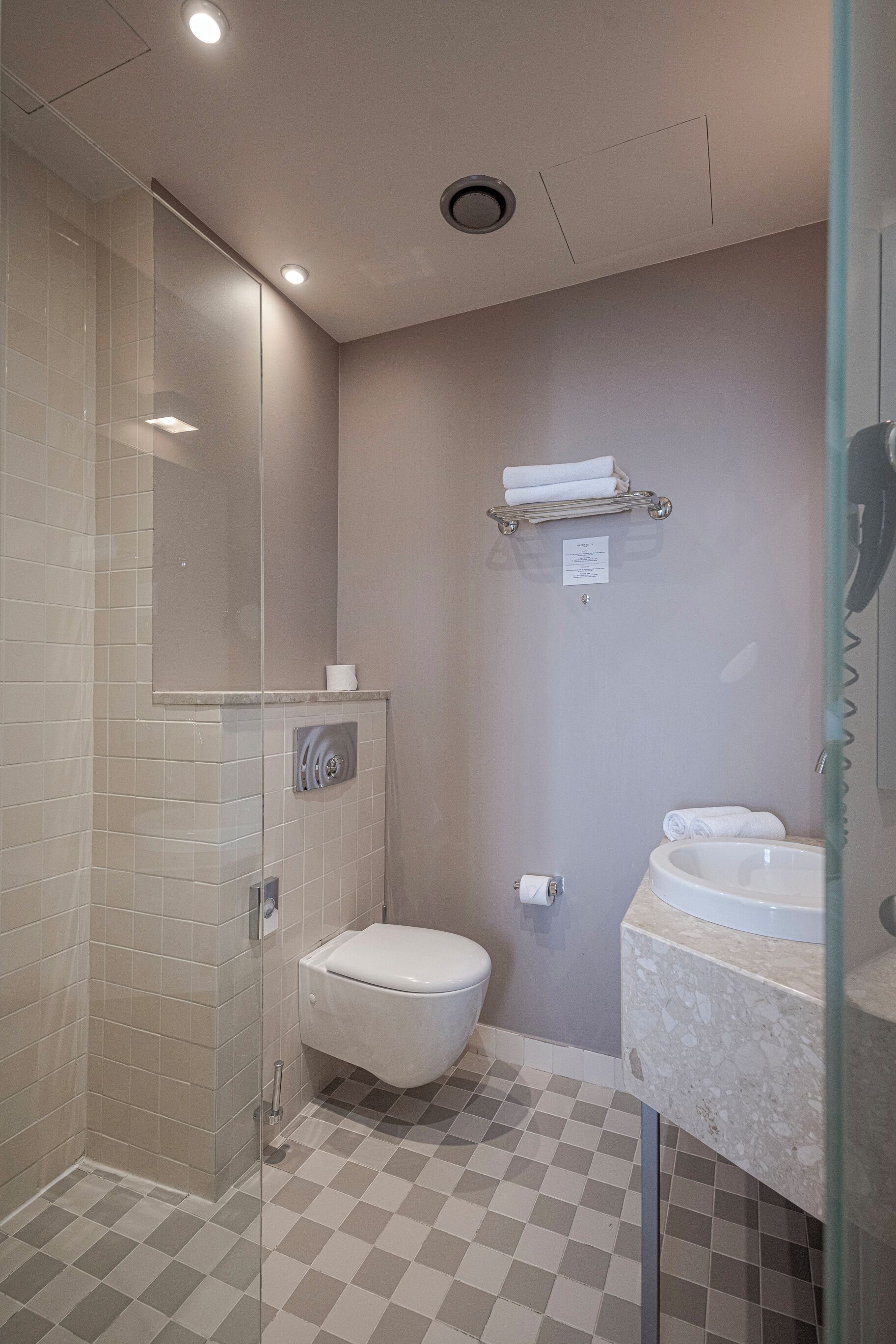 A bathroom with a glass shower enclosure, a toilet, a sink, and a towel rack.