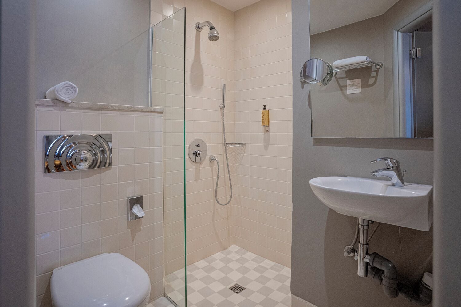 Un baño con cabina de ducha de vidrio, inodoro blanco, lavamanos con espejo y perchero para toallas.