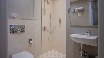 Un baño con cabina de ducha de vidrio, inodoro blanco, lavamanos con espejo y perchero para toallas.