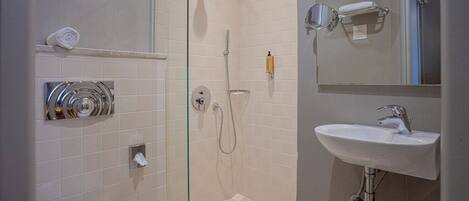 Un baño con cabina de ducha de vidrio, inodoro blanco, lavamanos con espejo y perchero para toallas.