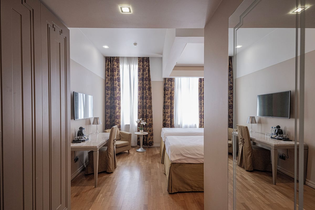 A hotel room with a bed, a desk, a chair, a TV, and a window with curtains.