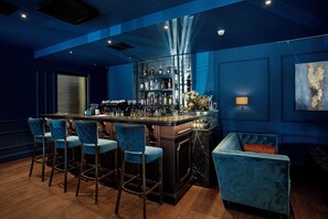Un espace bar doté d’un comptoir en marbre, de tabourets de bar et d’un coin salon avec un fauteuil en velours.
