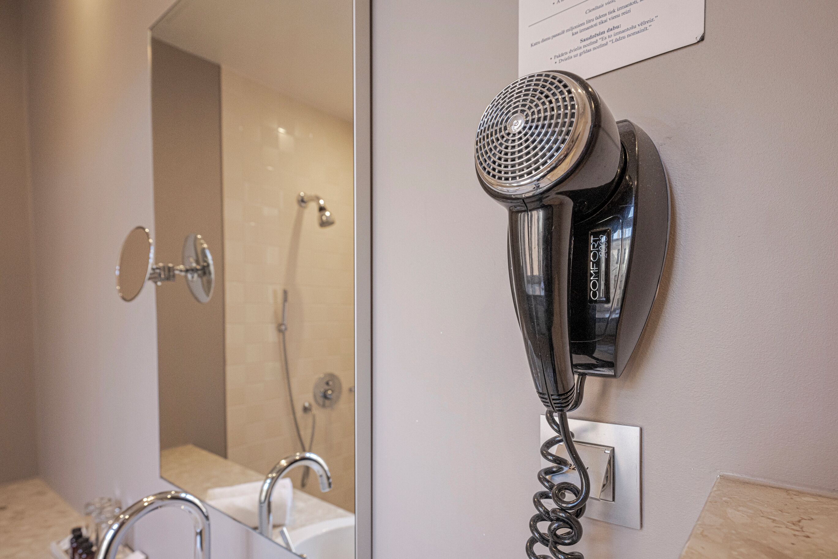 A hairdryer mounted on a wall in a bathroom with a mirror, sink, and shower.