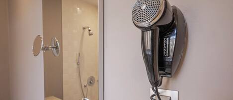 A hairdryer mounted on a wall in a bathroom with a mirror, sink, and shower.