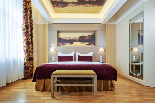 A hotel room with a large bed, two bedside lamps, a bench, and a large window with curtains.