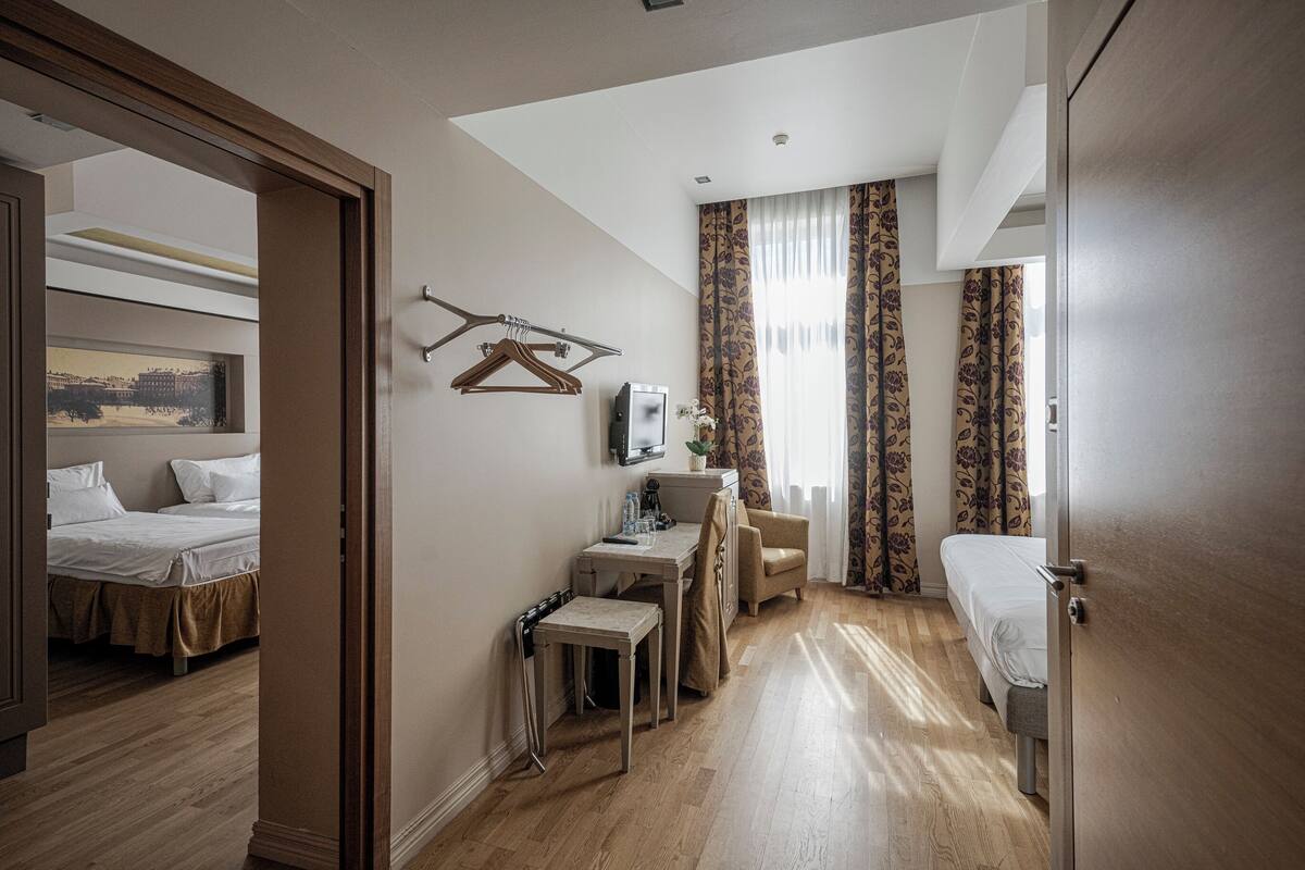A hotel room with a bed, a desk with a chair, a television, and a window with curtains.
