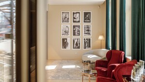 Une chambre d’hôtel avec un fauteuil rouge, une petite table, une lampe et un mur orné de tableaux.