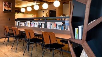 A modern interior with a wooden reception desk, black and orange chairs, and a bookshelf with books.