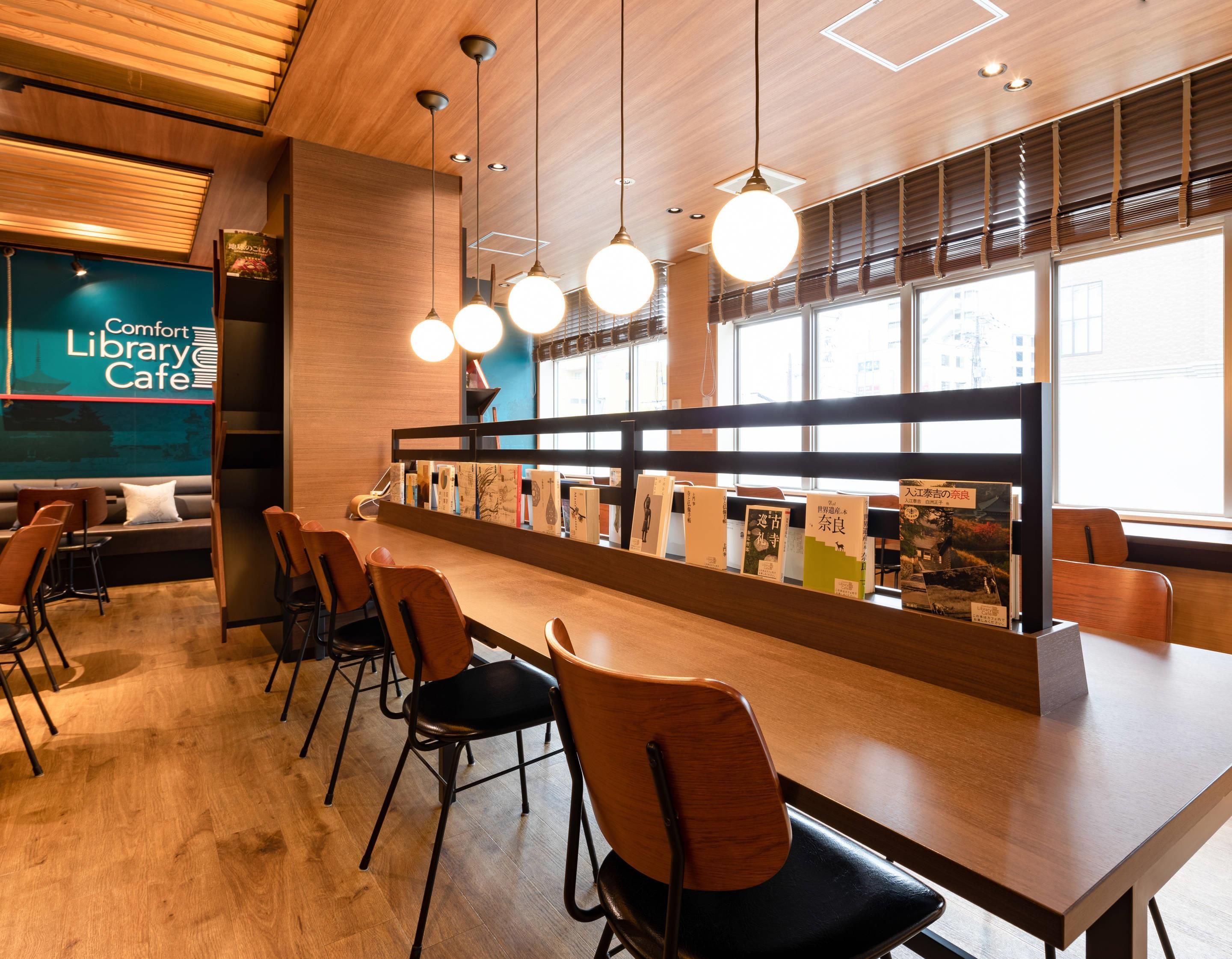 A library cafe with a long wooden table, chairs, and bookshelves.