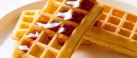 A close-up of a waffle with syrup being poured over it.