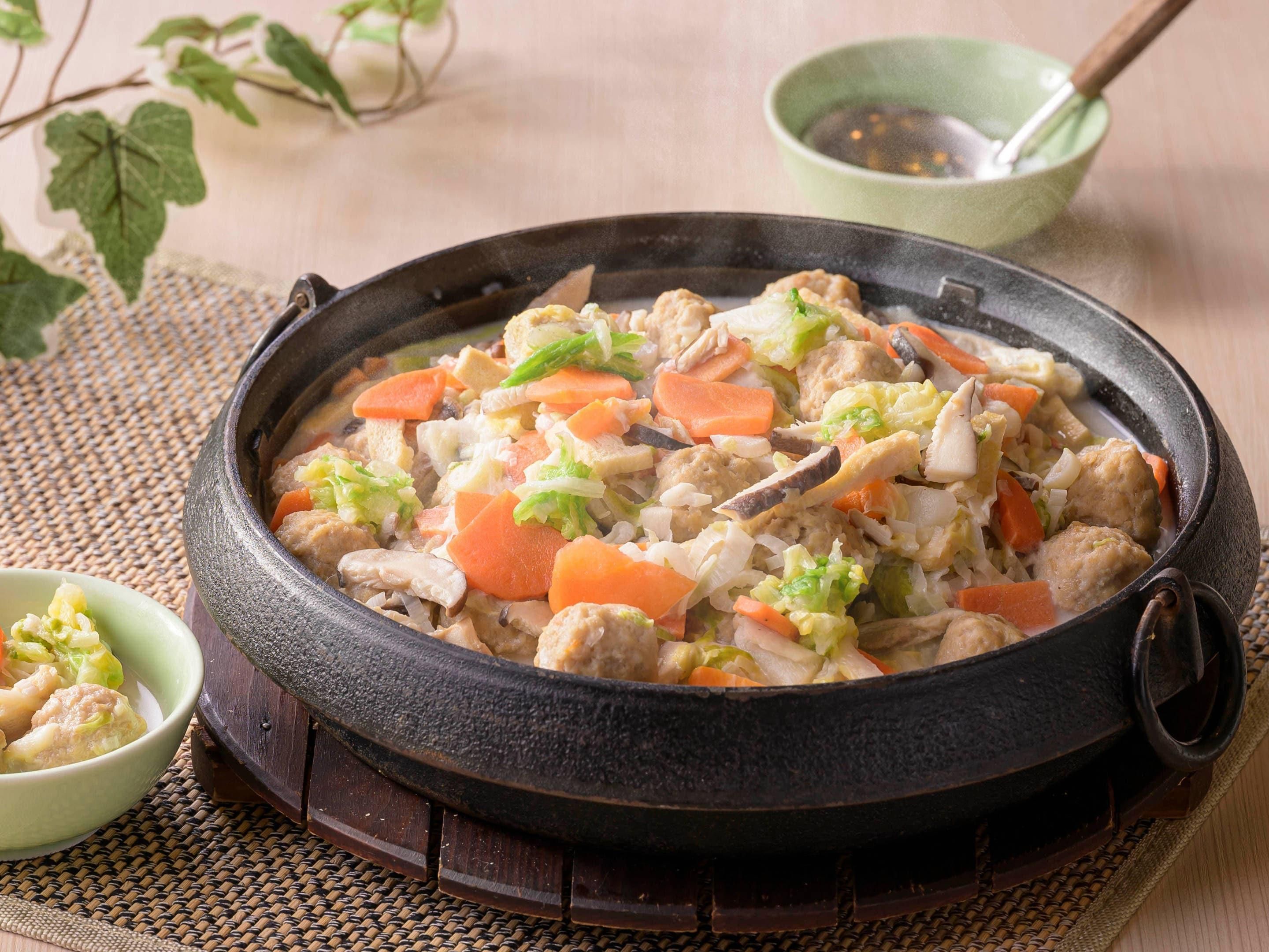 A traditional cooking pot filled with a stew containing meat, vegetables, and possibly tofu.