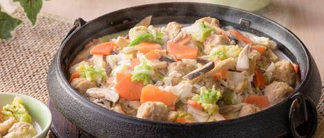 A traditional cooking pot filled with a stew containing meat, vegetables, and possibly tofu.