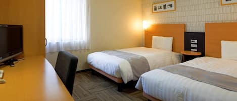 Habitación de hotel con dos camas, un escritorio, televisión y ventana con cortinas.
