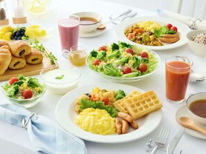 A breakfast buffet with various dishes including waffles, scrambled eggs, and a salad.