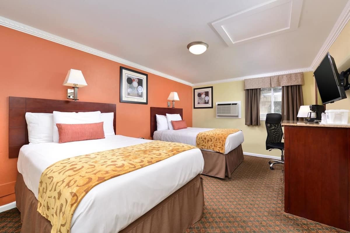 A hotel room with two beds, a desk, a television, and an air conditioning unit.