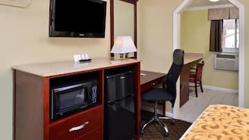A hotel room with a TV, microwave, refrigerator, desk, chair, and a bed with a patterned bedspread.