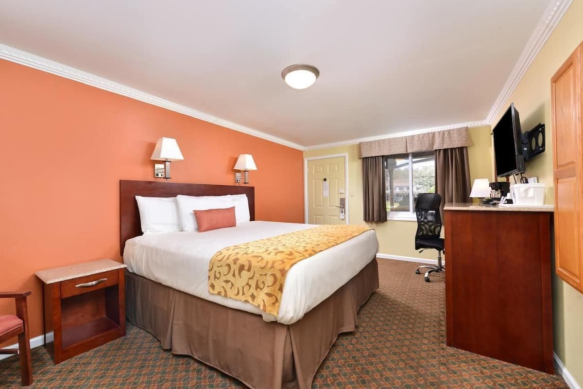 A hotel room with a bed, bedside lamps, a desk, a chair, a television, and a window with curtains.