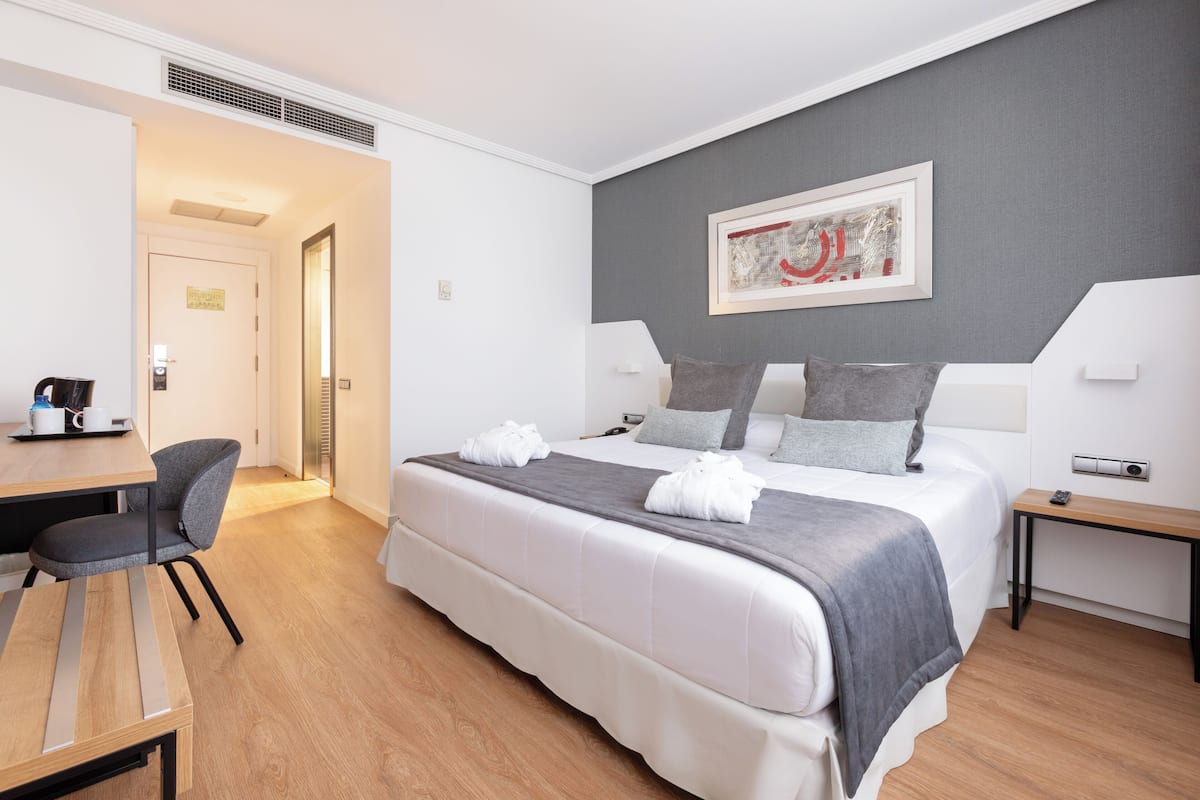 Une chambre d’hôtel comprenant un lit, un bureau, une chaise, une table de chevet et un tableau encadré au mur.