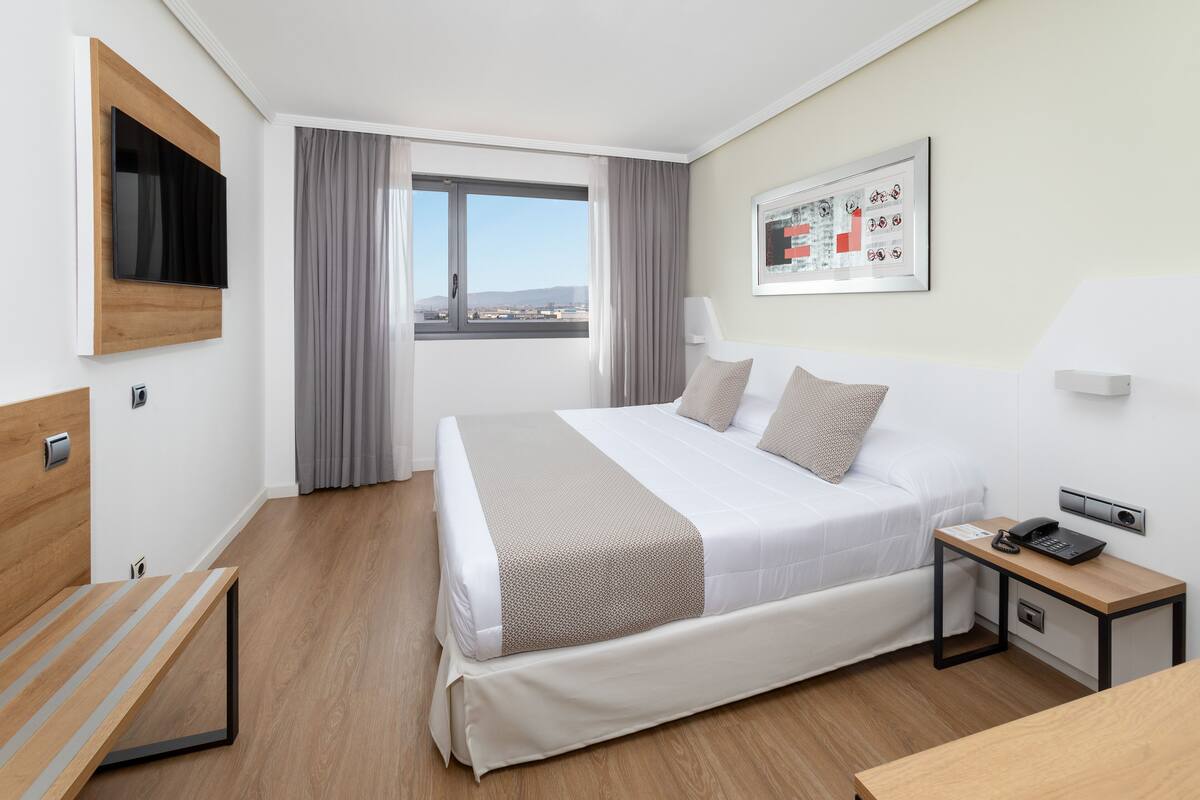 Ein modernes Hotelzimmer mit Bett, Nachttisch und einem fensterbepflanzten Fenster.