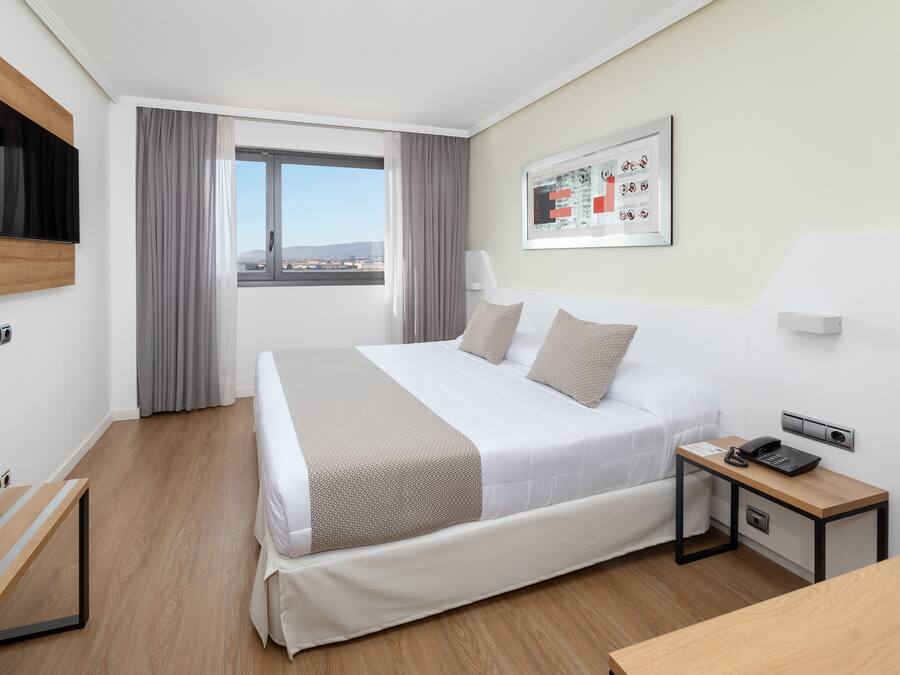 Une chambre d’hôtel moderne, équipée d’un lit, d’une table de chevet et d’une fenêtre avec des rideaux.