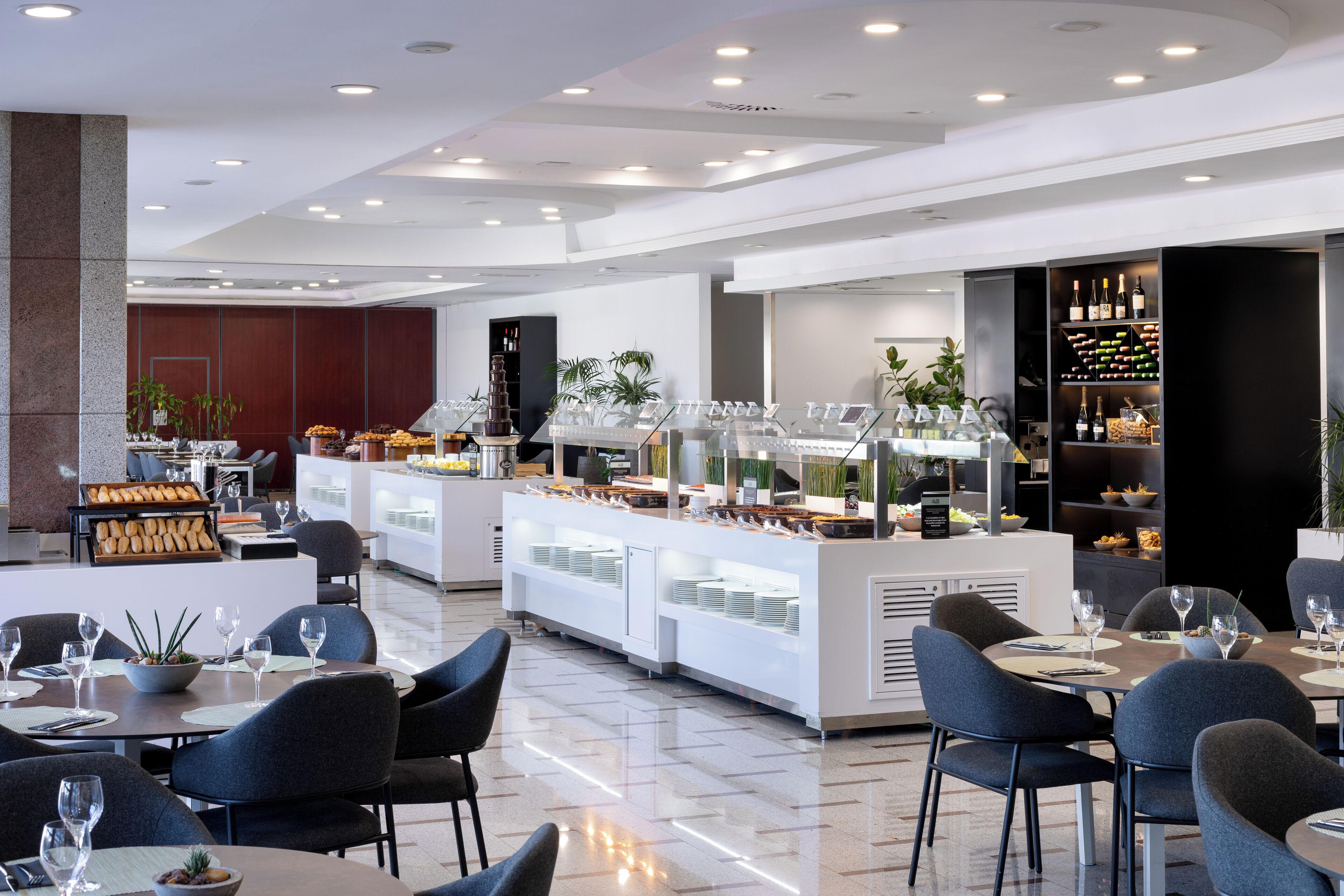 A modern hotel restaurant with a buffet area, seating, and a wine display.