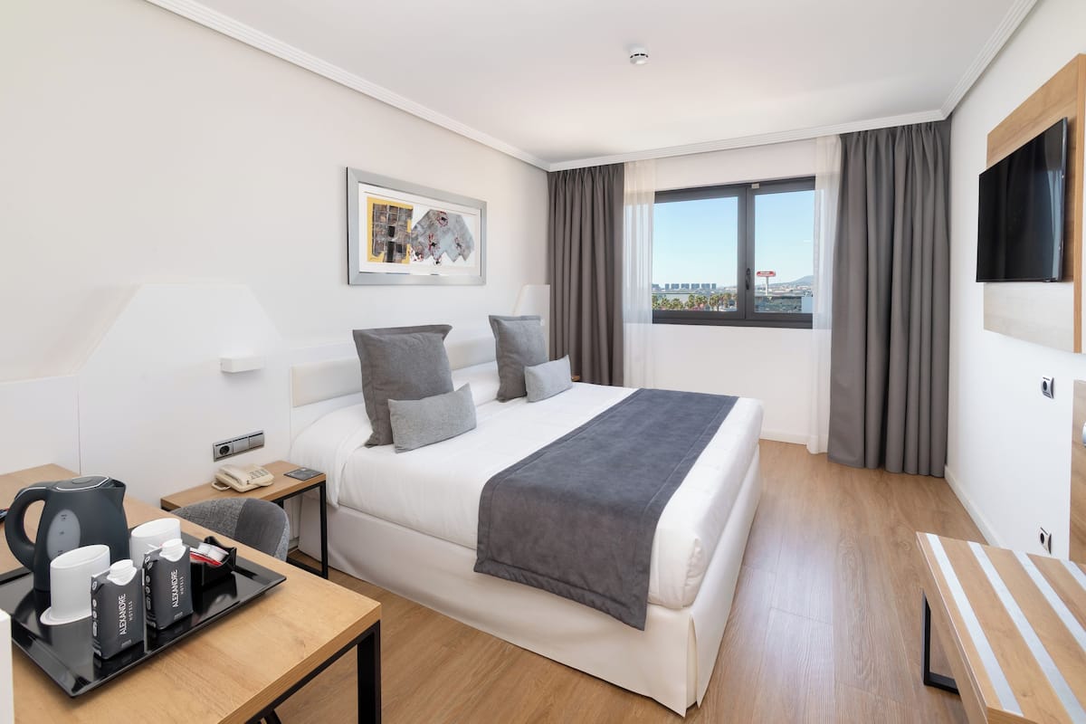 Ein Hotelzimmer mit Bett, Schreibtisch mit Kaffeemaschine, Fernseher und einem Fenster mit Vorhängen.