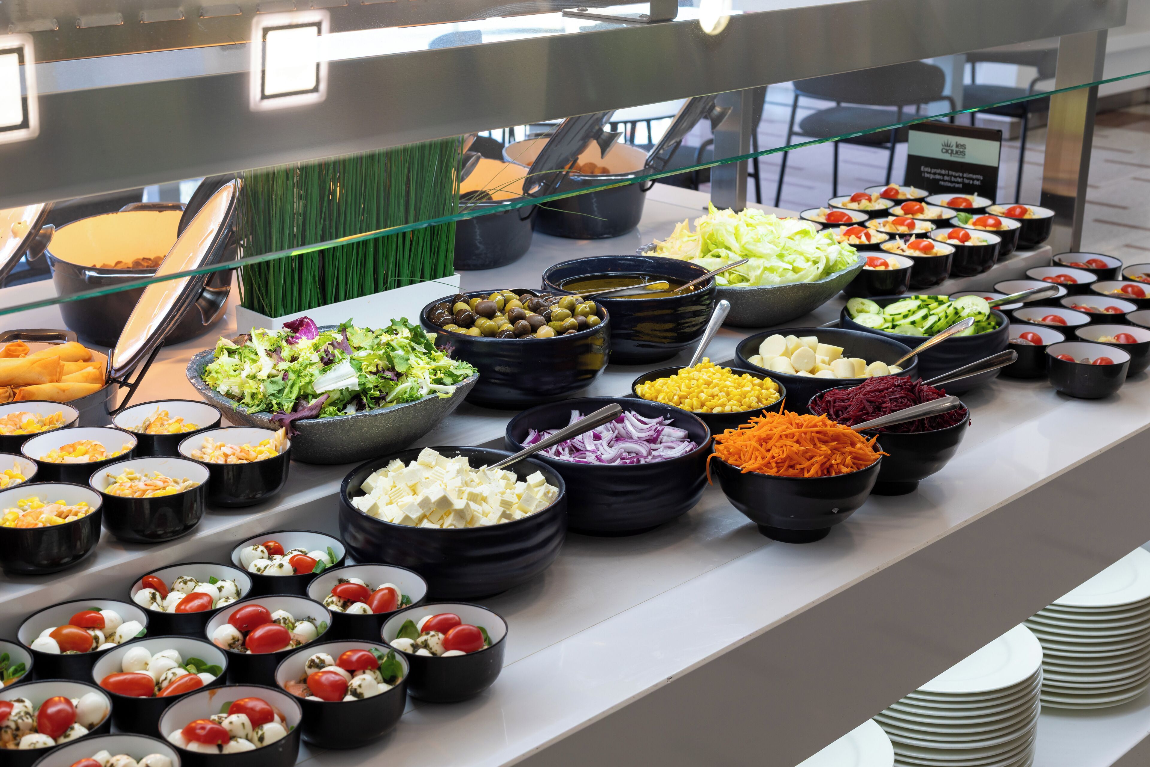 Un bufé con diversos alimentos en recipientes negros, como ensaladas, quesos y verduras.