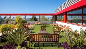 Une terrasse sur le toit avec une pelouse verdoyante, des meubles en bois et des chaises longues.
