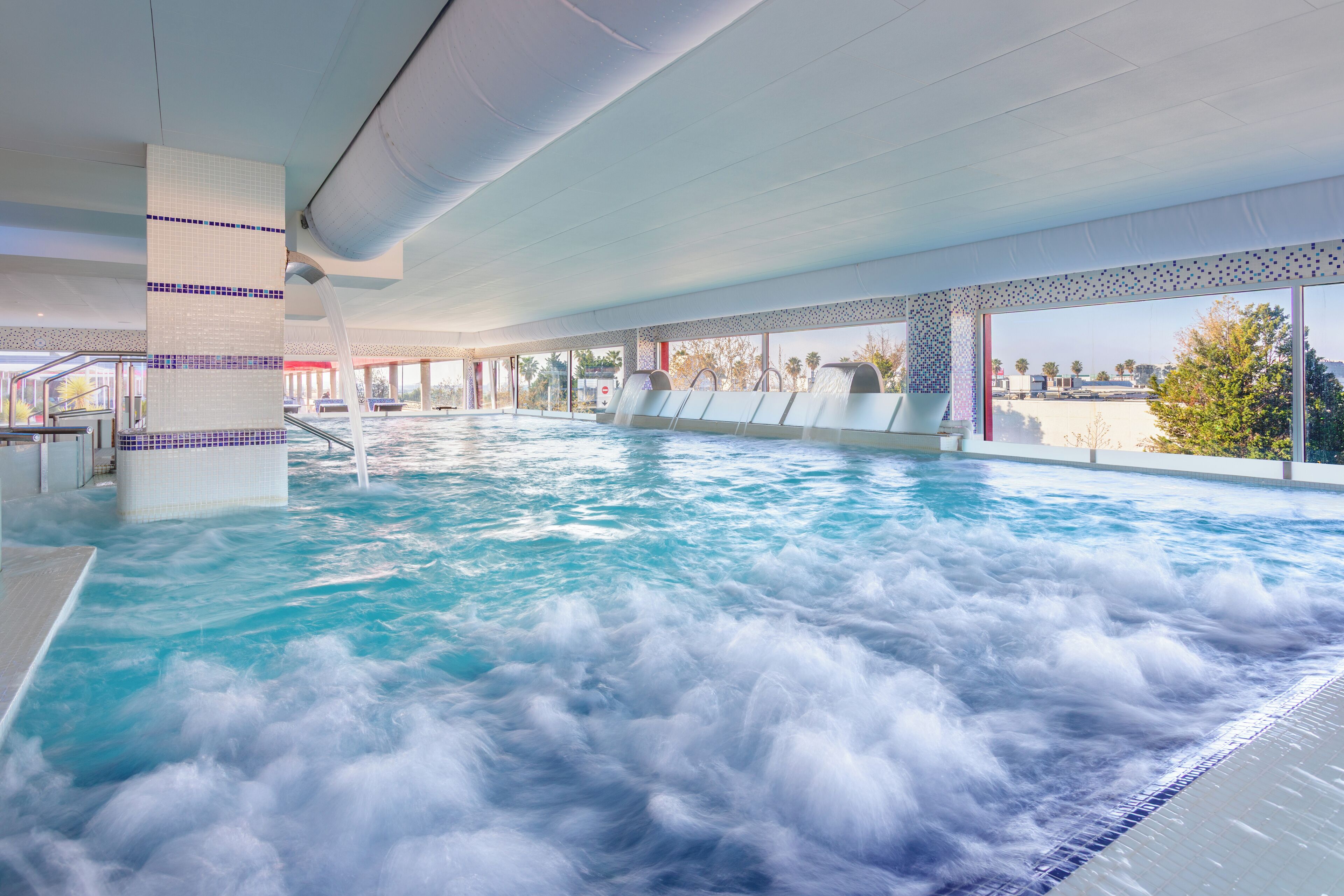 A large indoor swimming pool with multiple lanes, a water slide, and a view of the surrounding landscape.