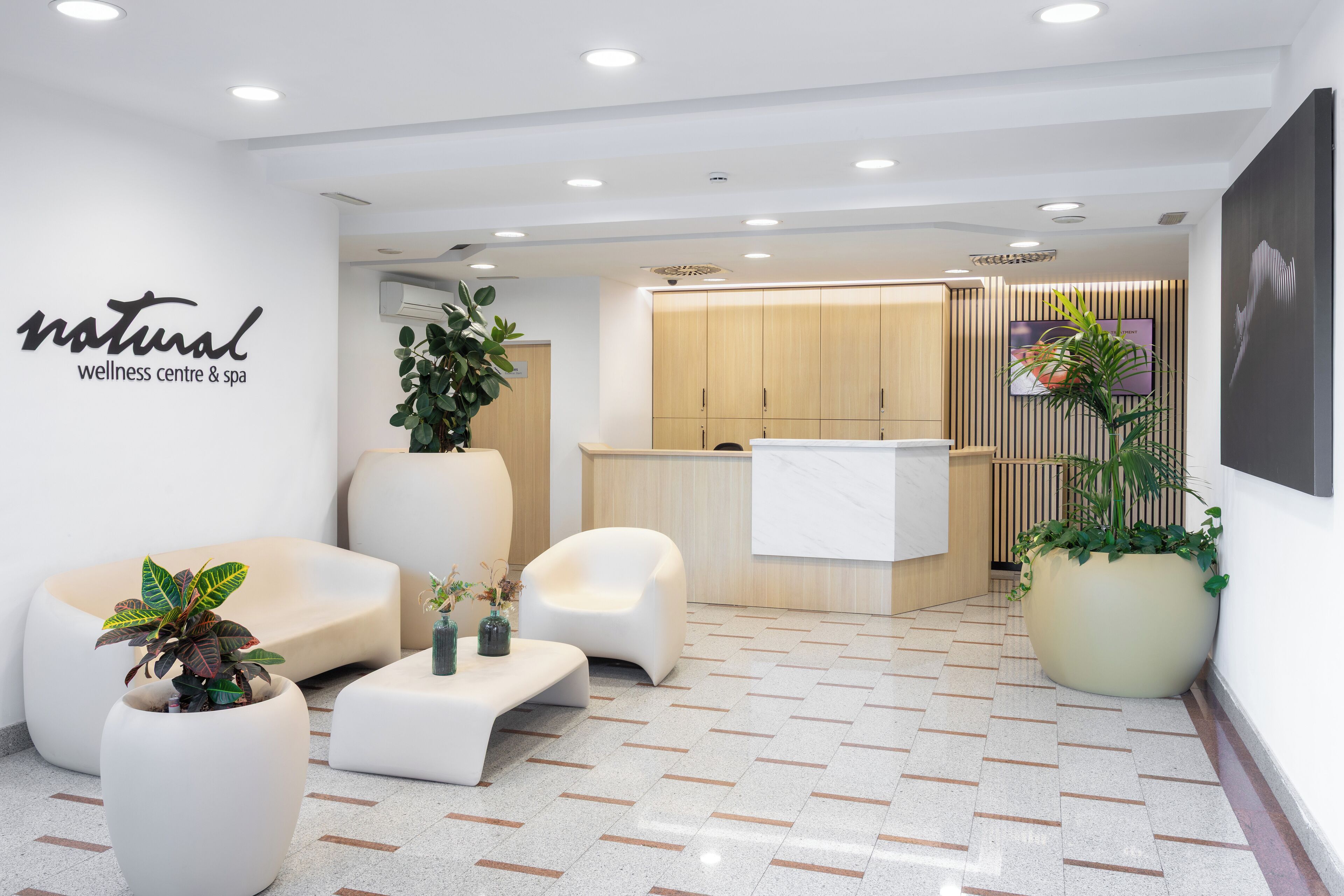 Un centre de bien-être moderne doté d’un comptoir d’accueil, d’un espace détente et de plantes en pot.