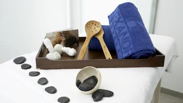 Un ambiente de spa con una bandeja de madera que contiene una toalla azul, una cuchara de madera, un libro titulado 'Chakra Stalk' y un cuenco de piedras negras.