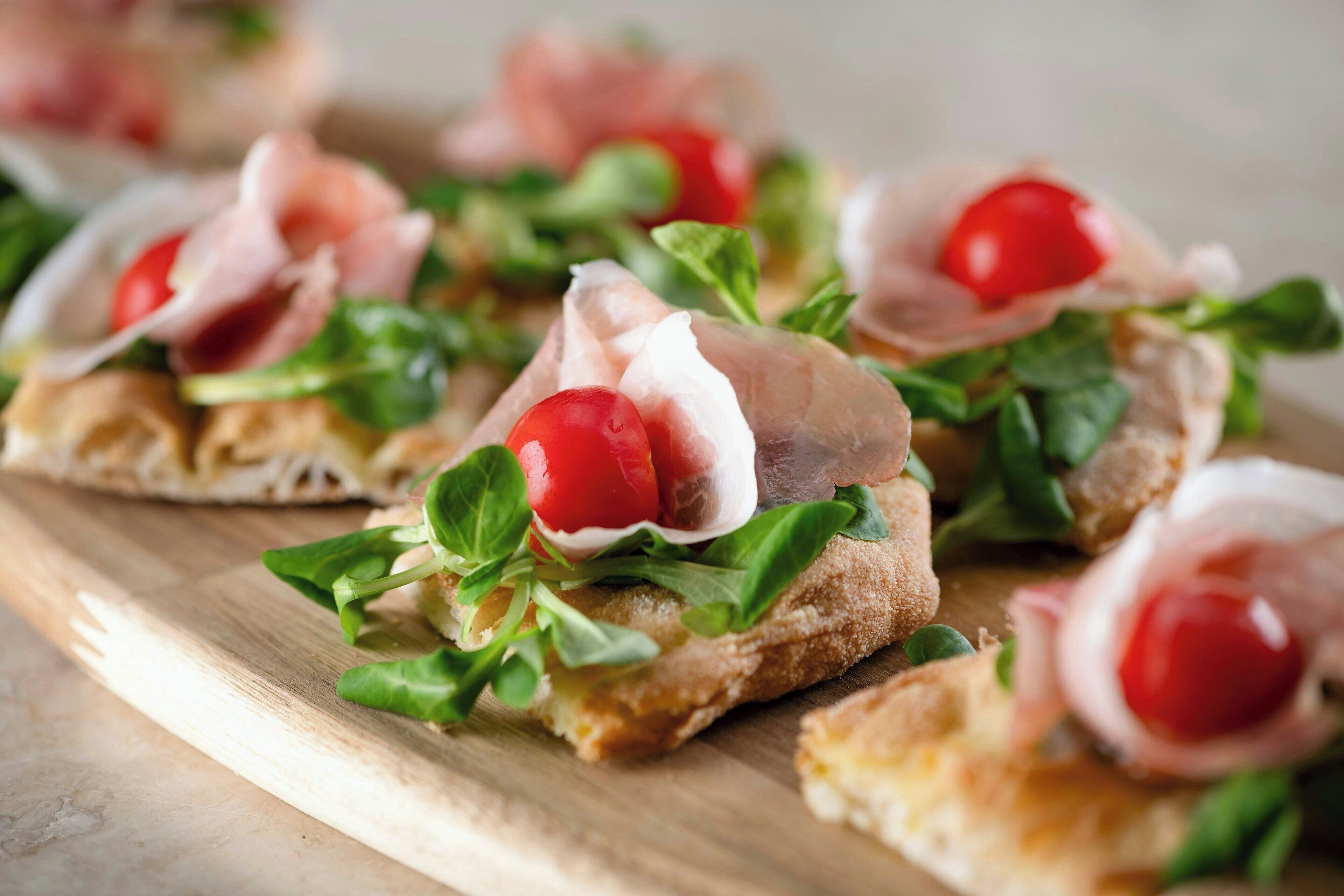 A wooden board with several appetizers consisting of bread, greens, and cherry tomatoes.