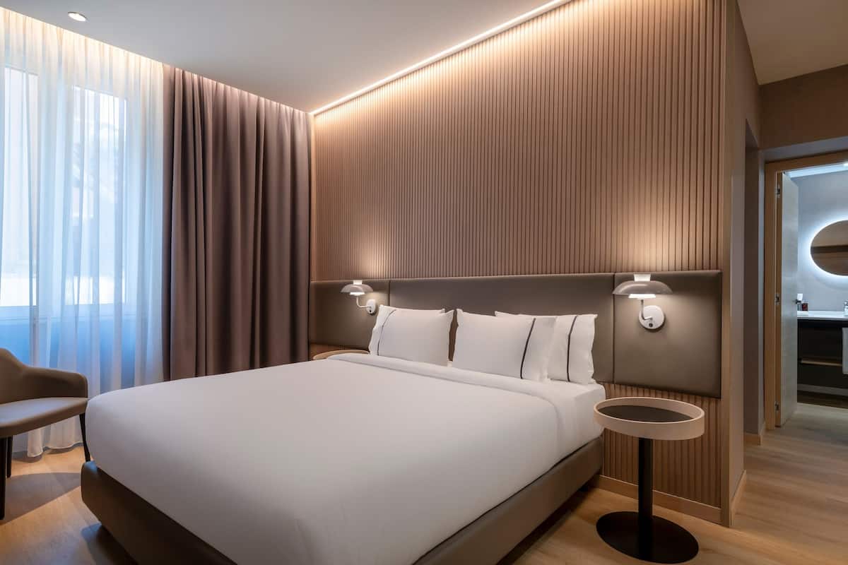 A modern hotel room with a large bed, a bedside table, and a chair.