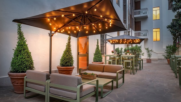 An outdoor seating area with tables and chairs, surrounded by potted plants and under large umbrellas.