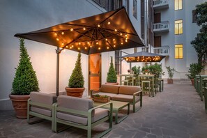 An outdoor seating area with tables and chairs, surrounded by potted plants and under large umbrellas. - AC Hotel by Marriott Clodio Roma (Rome)
