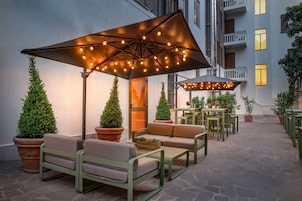 An outdoor seating area with tables and chairs, surrounded by potted plants and under large umbrellas.