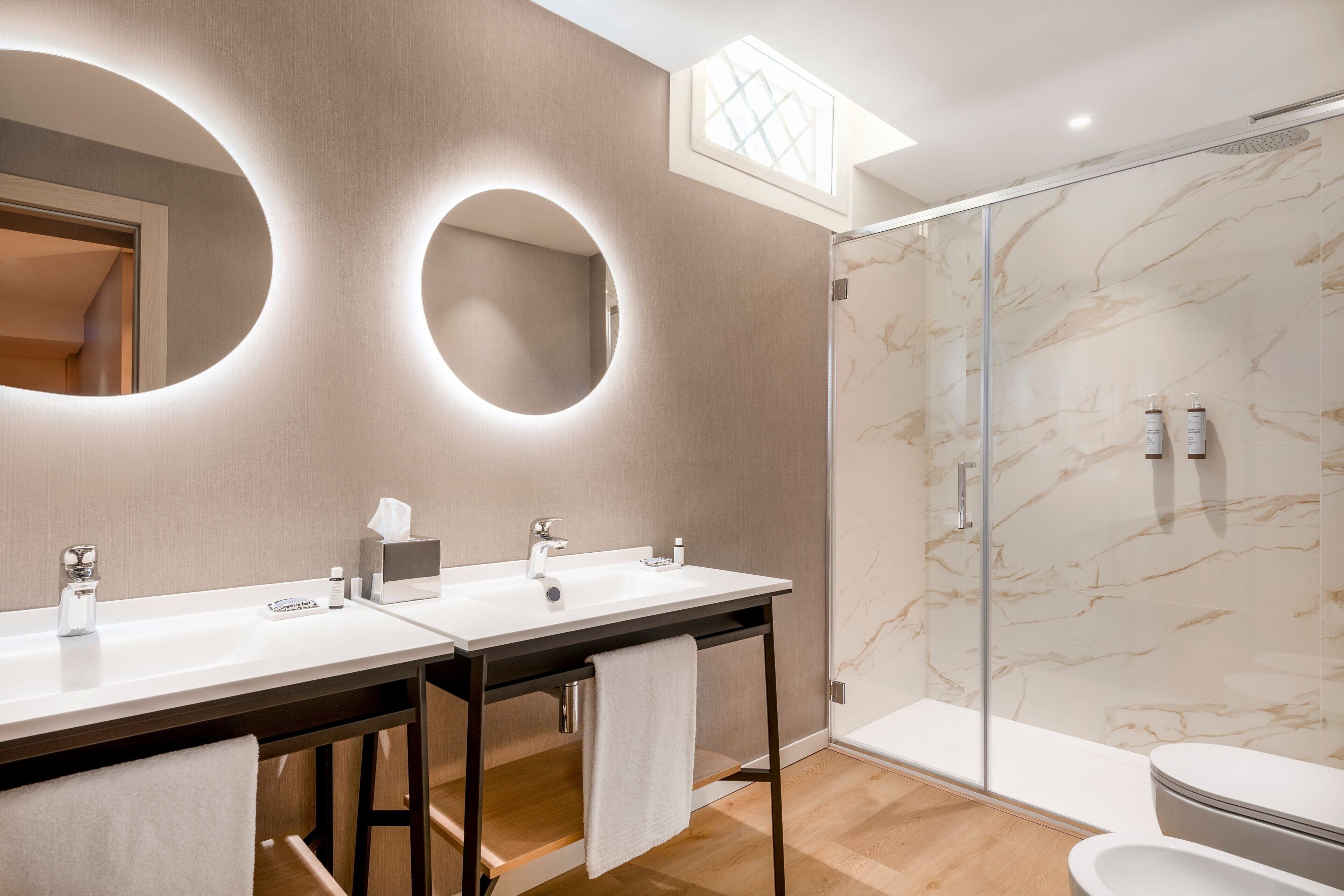 A modern bathroom with two sinks, a glass shower enclosure, and a marble wall.