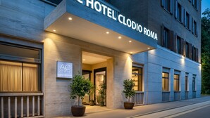 The exterior of AC Hotel Clodio Roma with a modern facade, large potted plants, and a well-lit entrance.