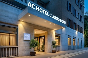 The exterior of AC Hotel Clodio Roma with a modern facade, large potted plants, and a well-lit entrance.