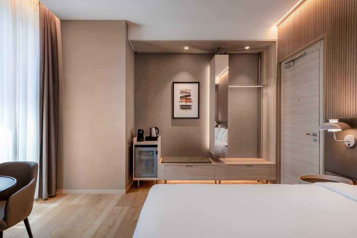A modern hotel room with a bed, bedside table, and a small kitchenette.